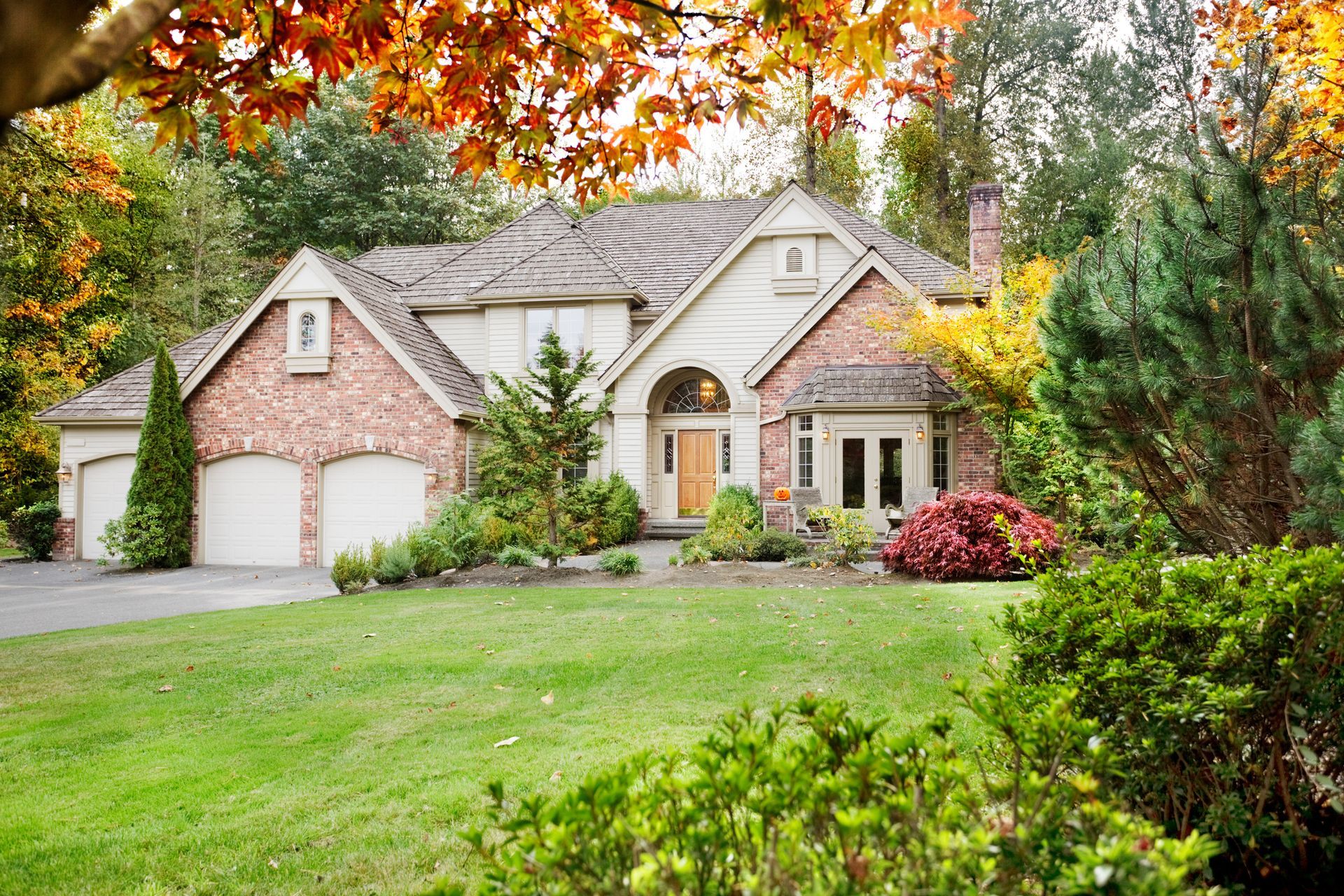 A large brick house with two garages is surrounded by trees and bushes.