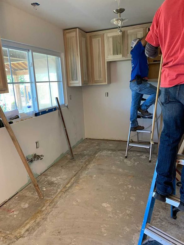 Two men are standing on ladders in a kitchen.