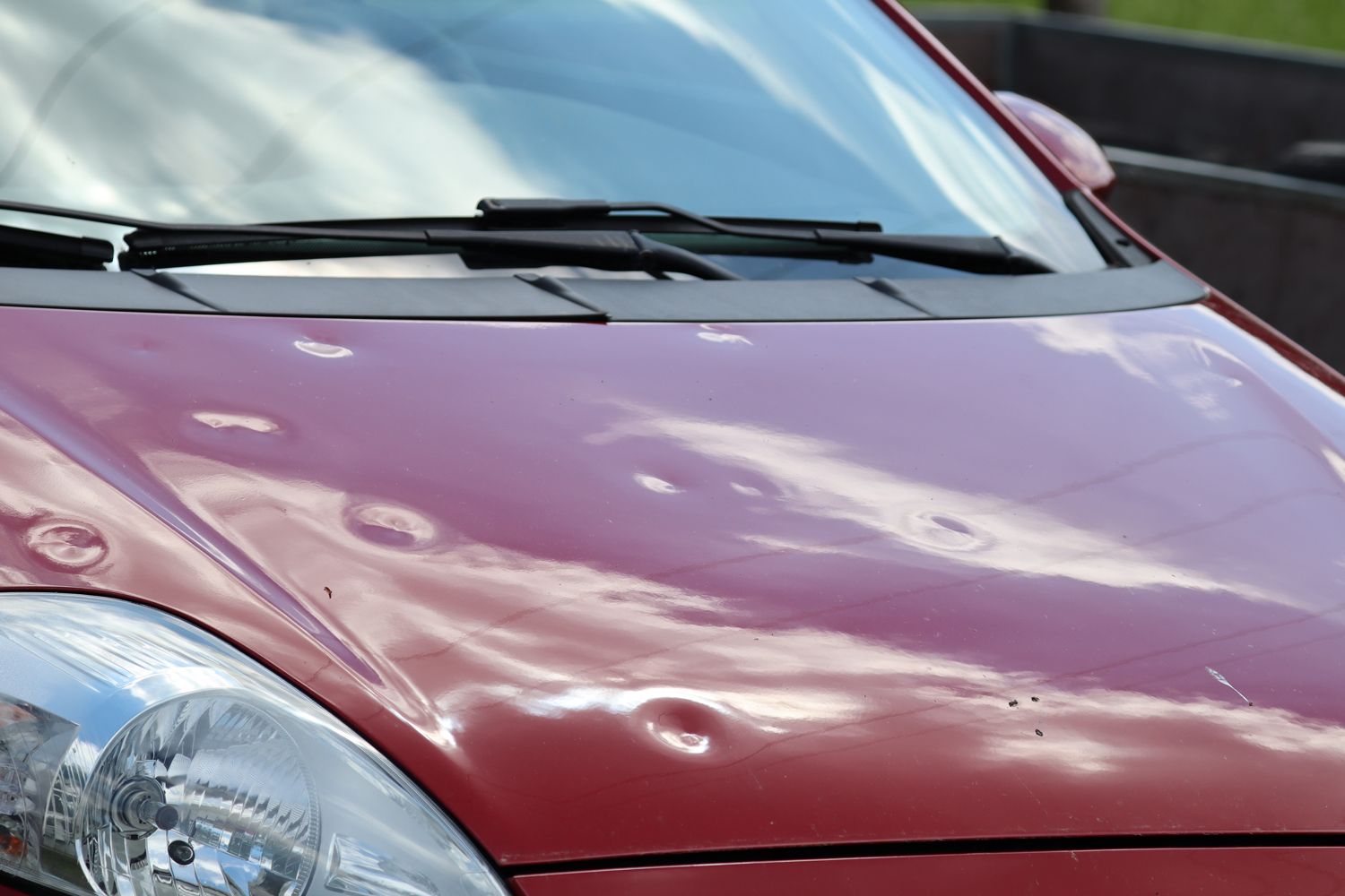 A close up of a red car with dents on the hood
