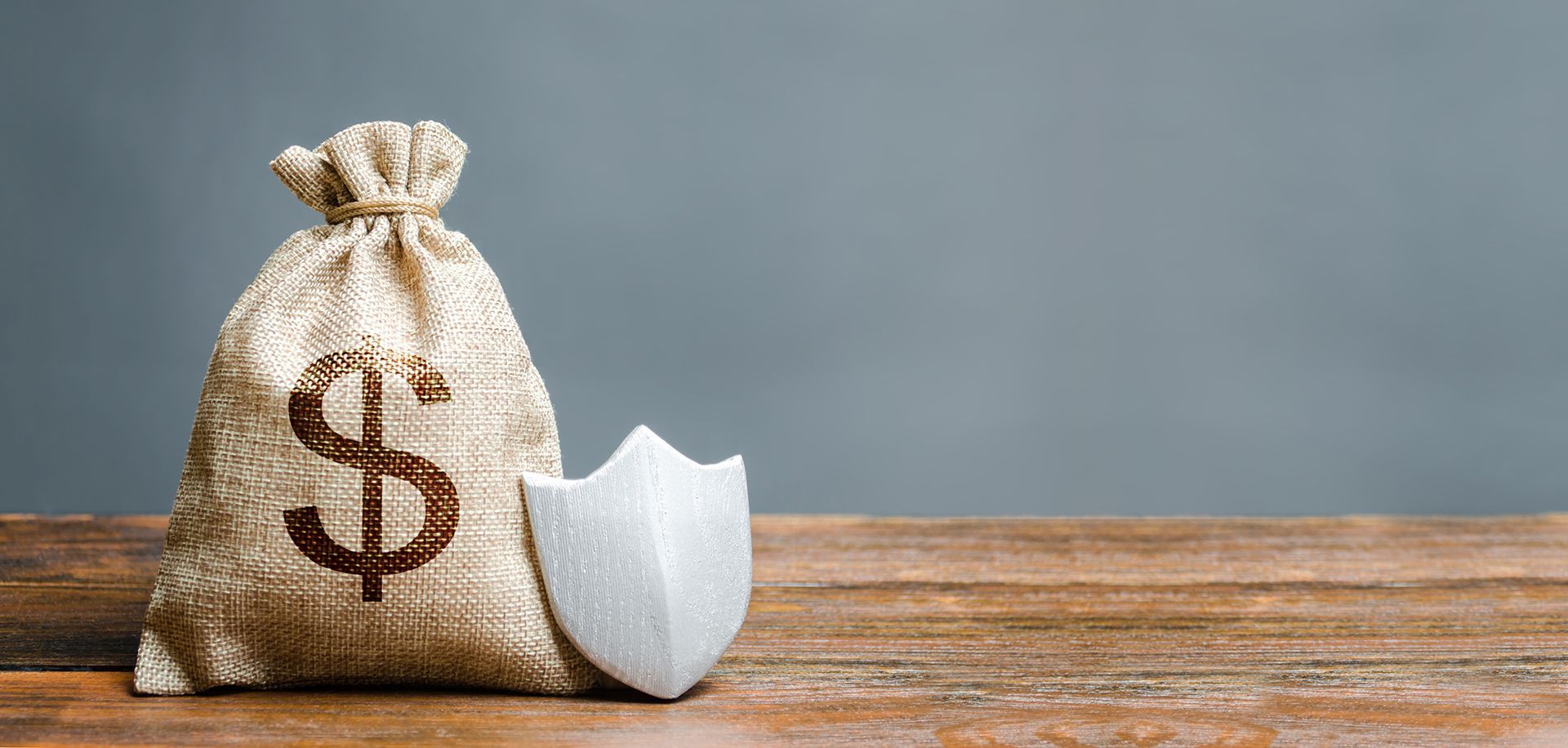 A money bag with a dollar sign on it and a shield on a wooden table.