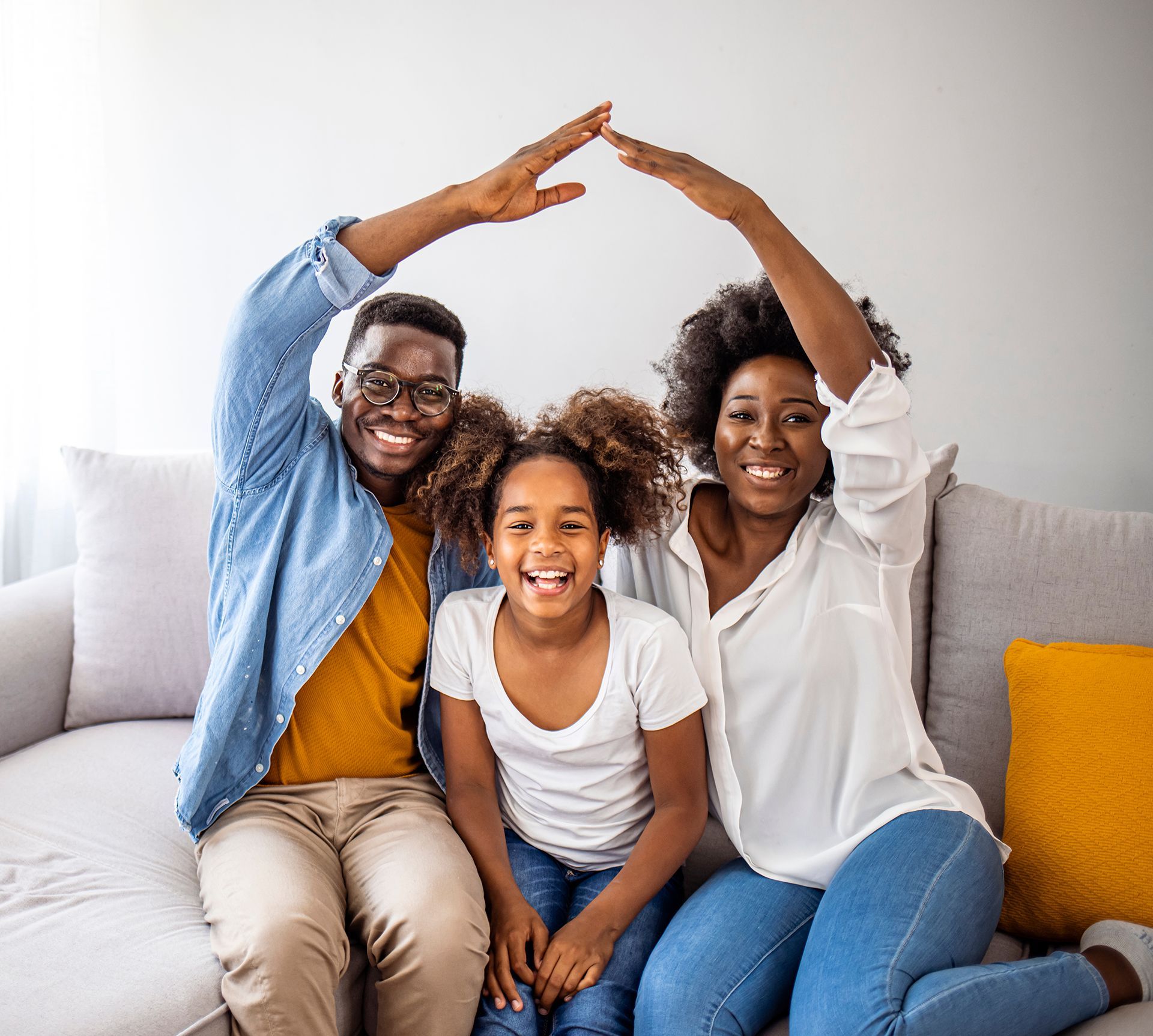 A family is sitting on a couch with their hands in the shape of a house.