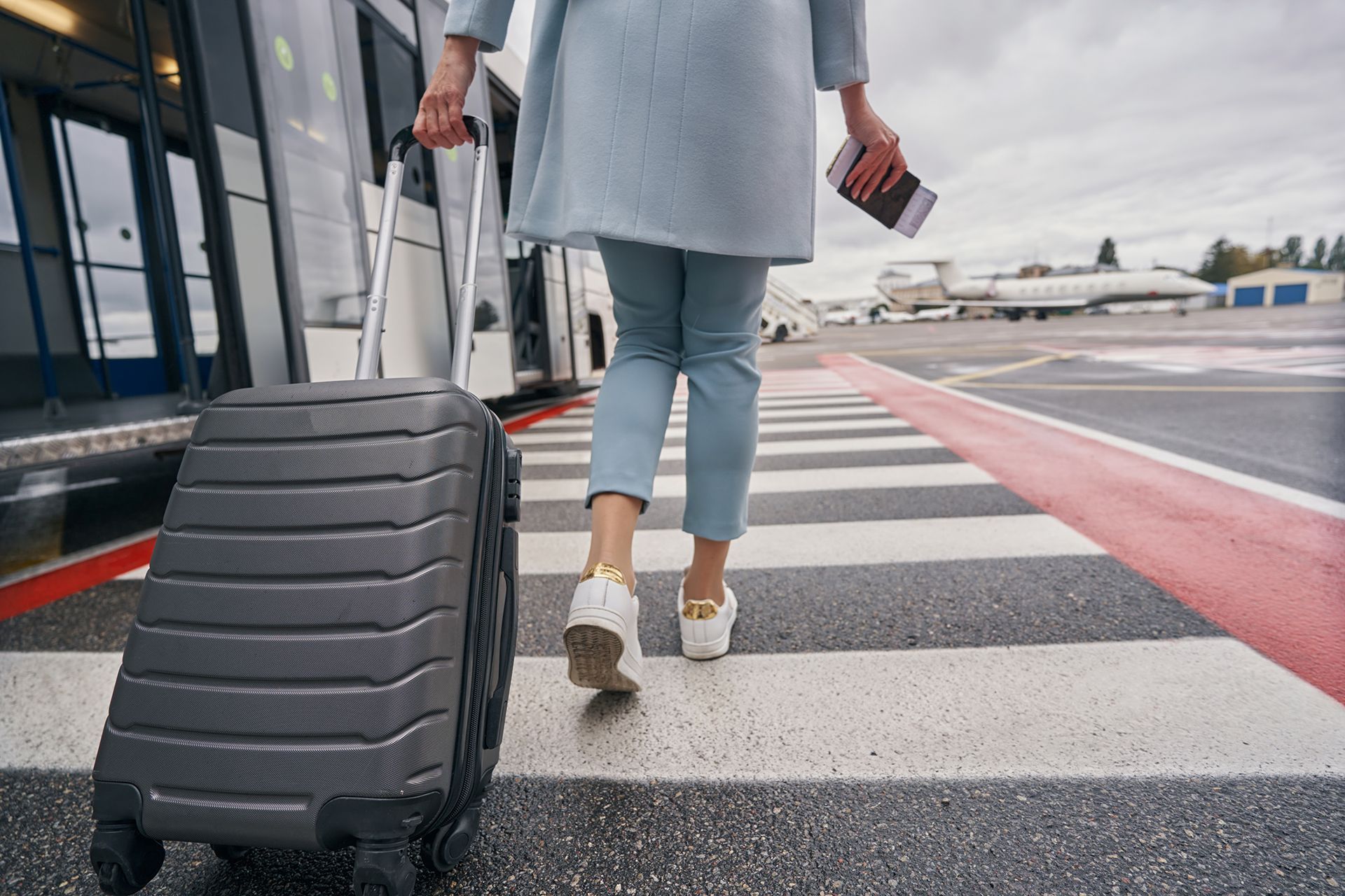 A woman is walking with a suitcase and a passport.