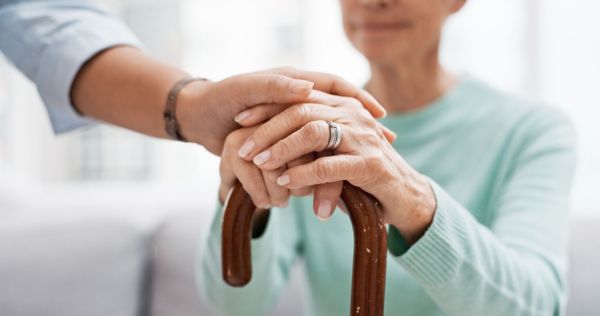 A person is holding the hand of an elderly woman holding a cane.