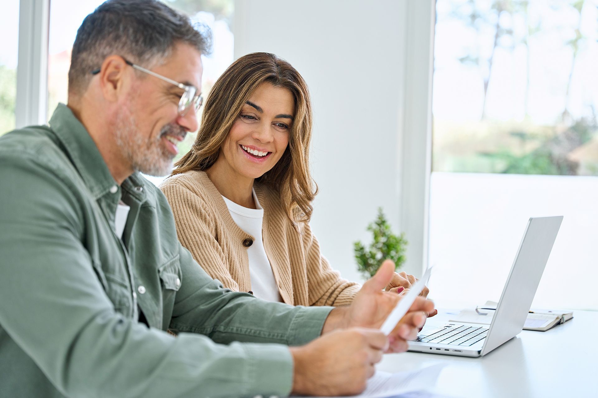 A man and a woman are sitting at a table looking at a laptop.