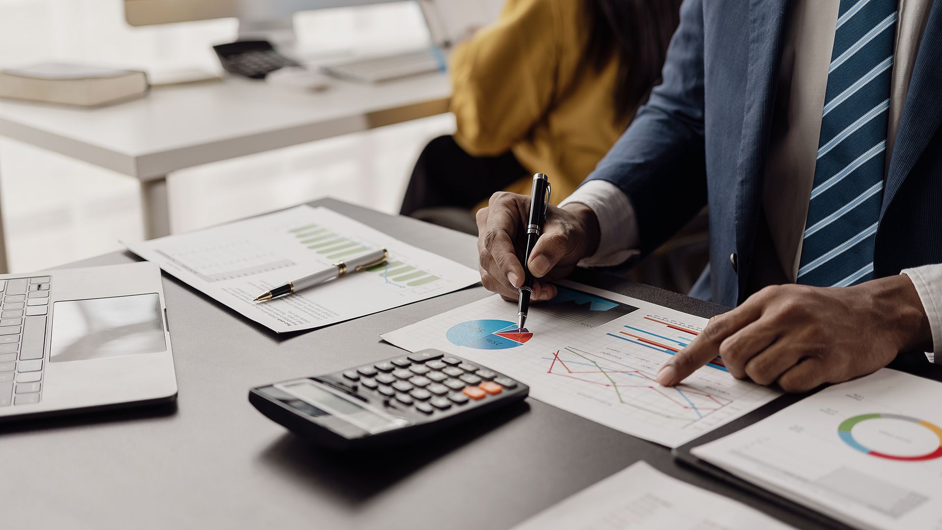 A man is sitting at a desk with a calculator and a pen.