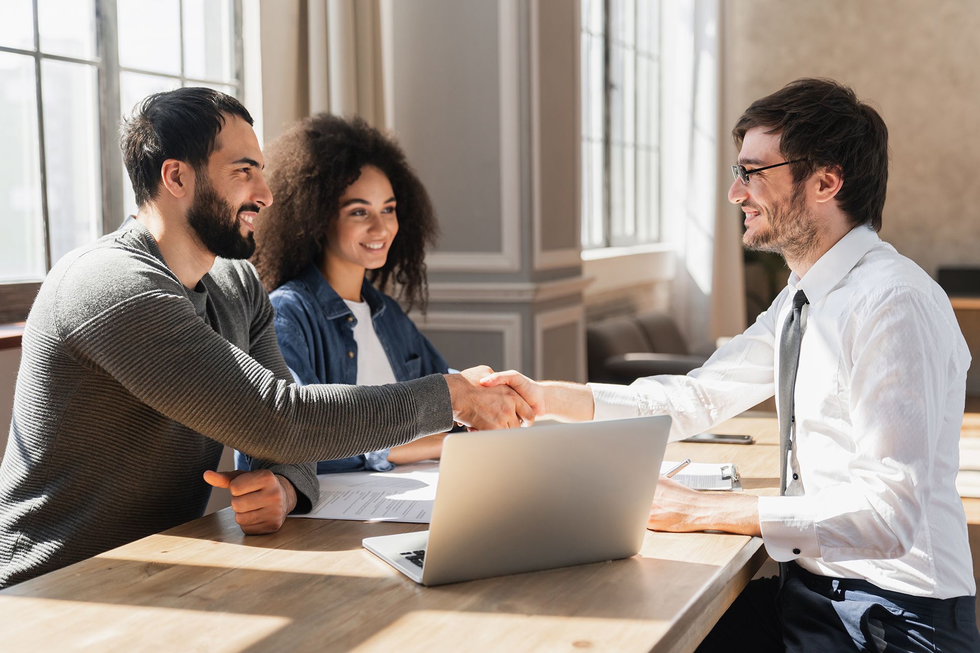 A man and woman are shaking hands with a man while sitting at a table with a laptop.