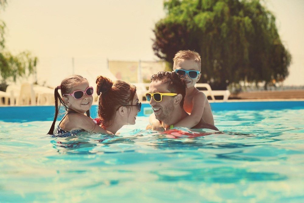 Family of Four in a Swimming Pool, Smiling and Wearing Sunglasses — Port Douglas Pool Shop in Craiglie, QLD
