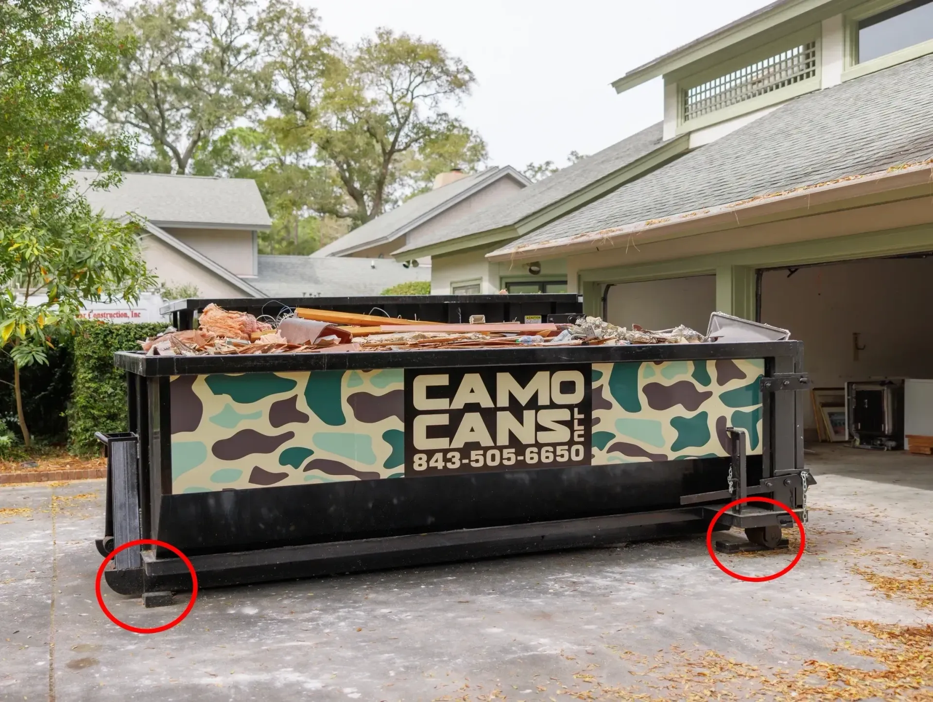 A dumpster with a camouflage design is parked in front of a house.