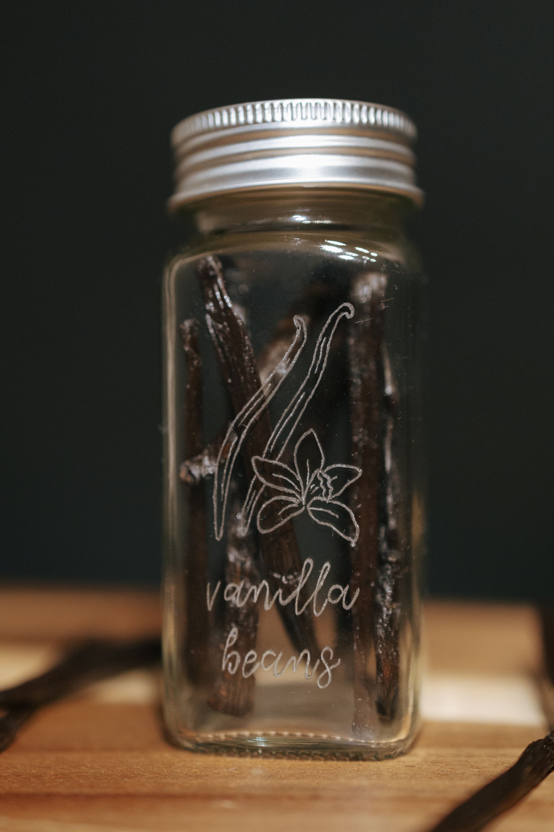 Jar of vanilla beans with etched design and silver lid.