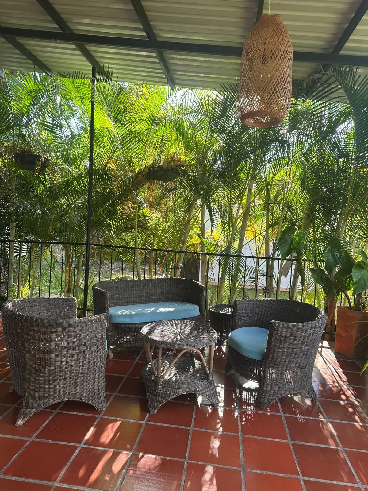 Patio al aire libre con muebles de mimbre, piso de baldosas rojas y una lámpara tejida.