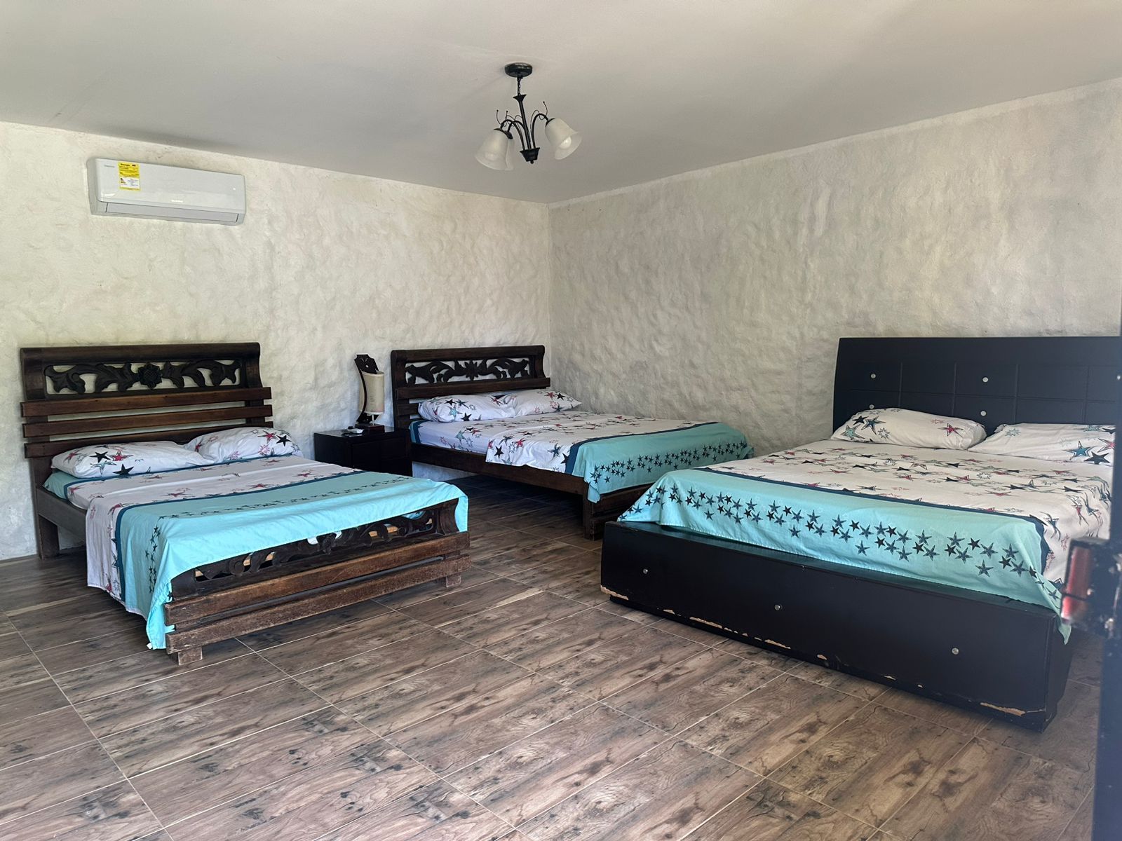 Dormitorio con tres camas, paredes texturizadas blancas, piso color claro, aire acondicionado.