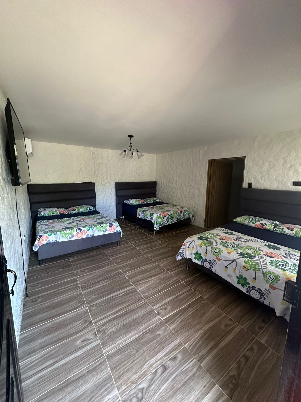 Tres camas en una habitación con paredes blancas texturizadas y piso de baldosas con apariencia de madera.