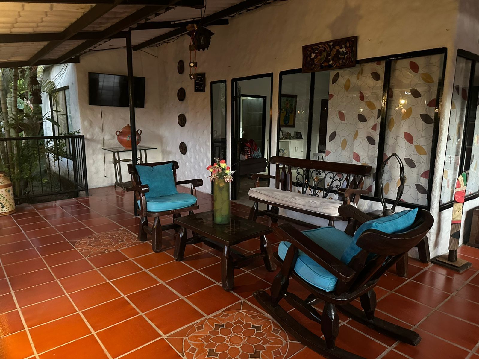 Patio cubierto con piso de baldosas naranjas, muebles de madera oscura y cojines azules.