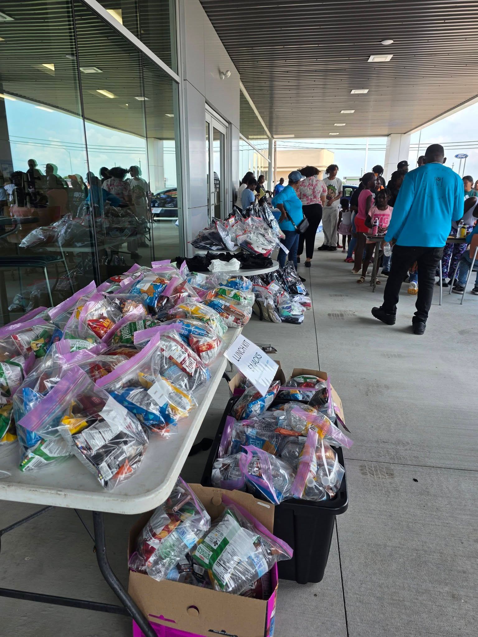 Tables lined with bagged donations under a covered outdoor walkway with people gathered nearby.