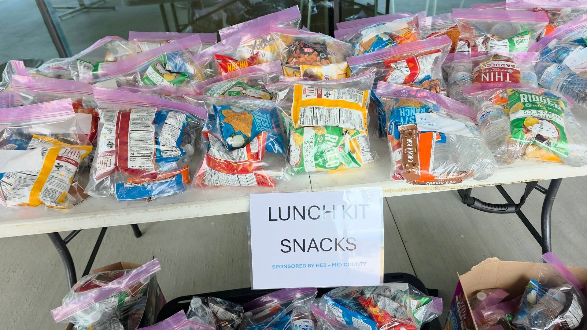 A white table filled with plastic bags of various snacks, with a sign reading 