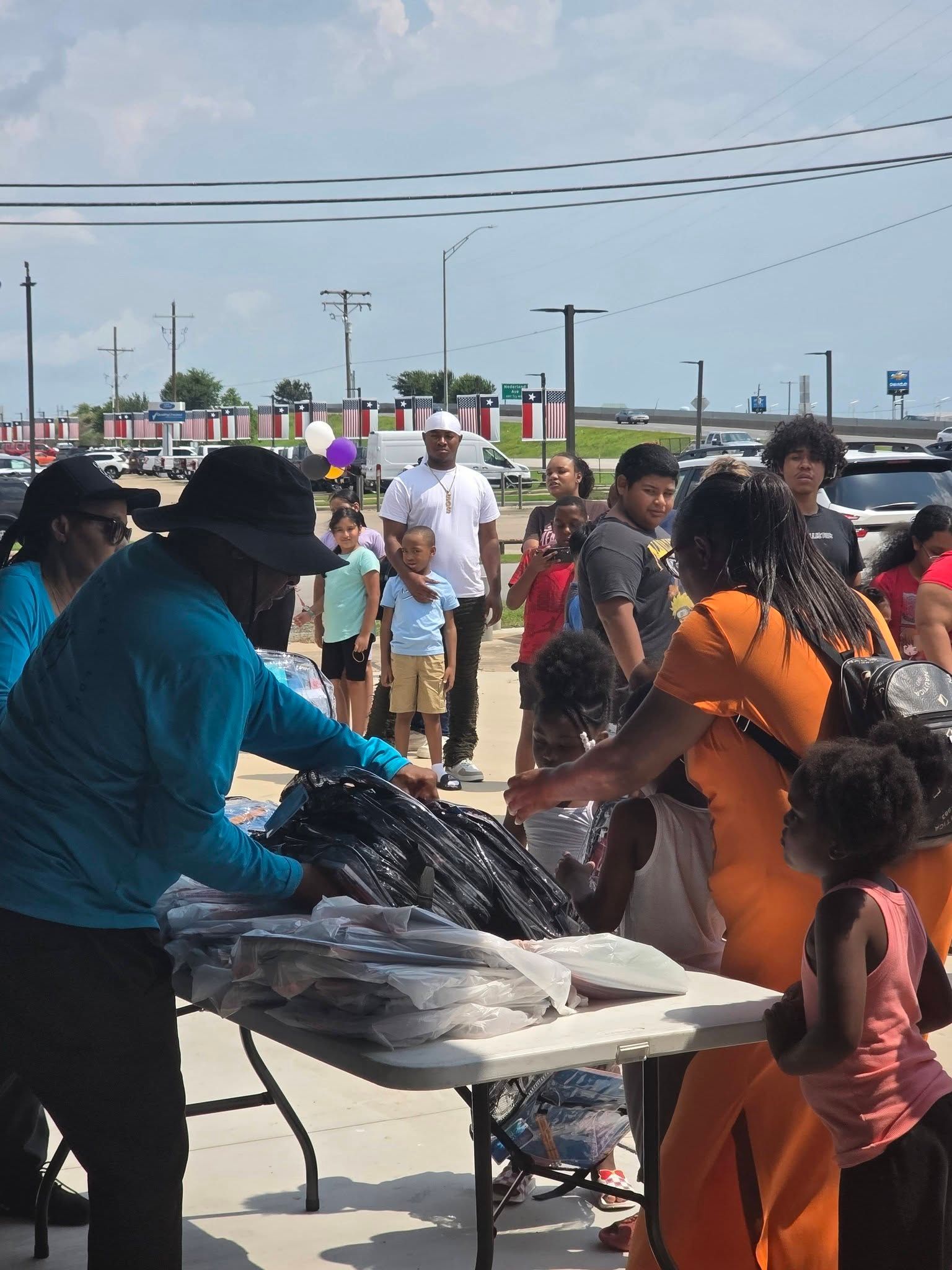 People hand out supplies from a table at an outdoor event on a sunny day.