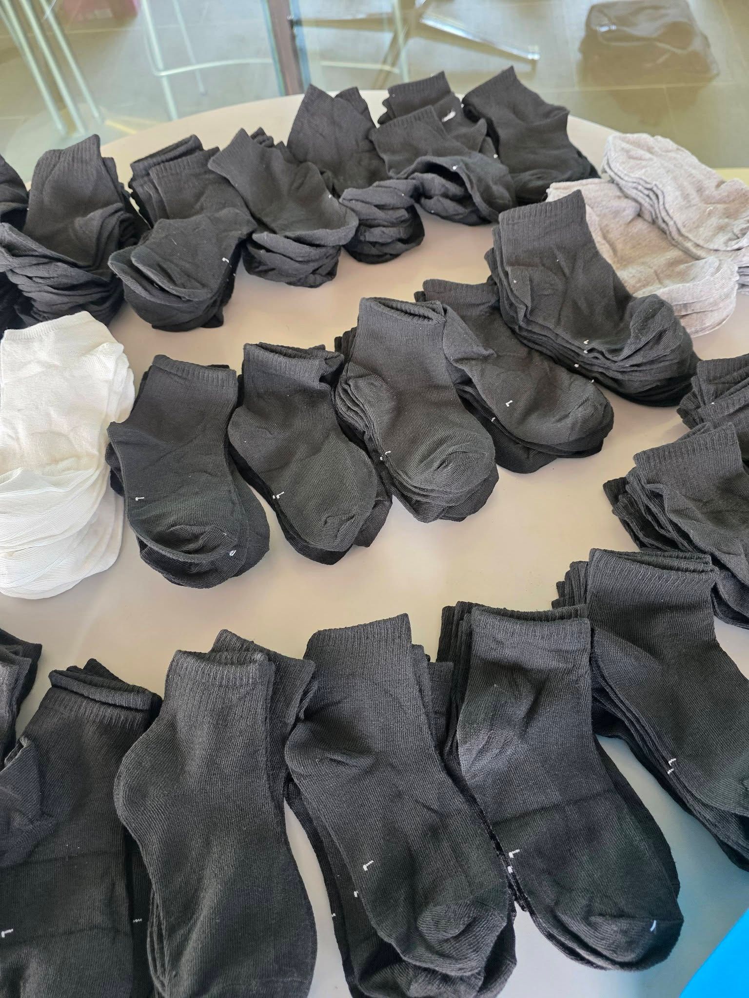 Stacks of dark grey ankle socks are arranged on a light-colored surface, with some white socks visible on the sides.