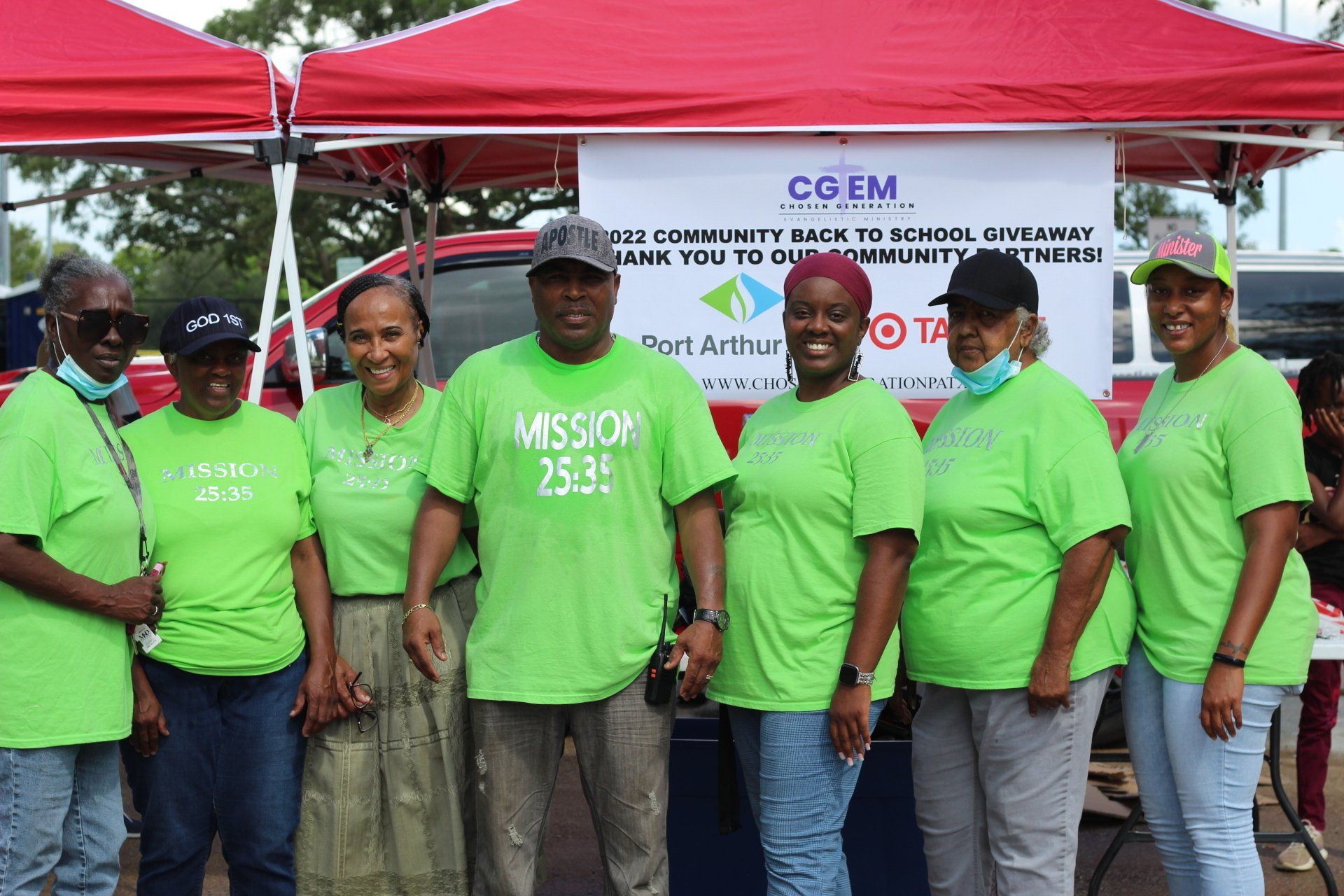 Group of people in green shirts pose at a community event with a banner and red tent.
