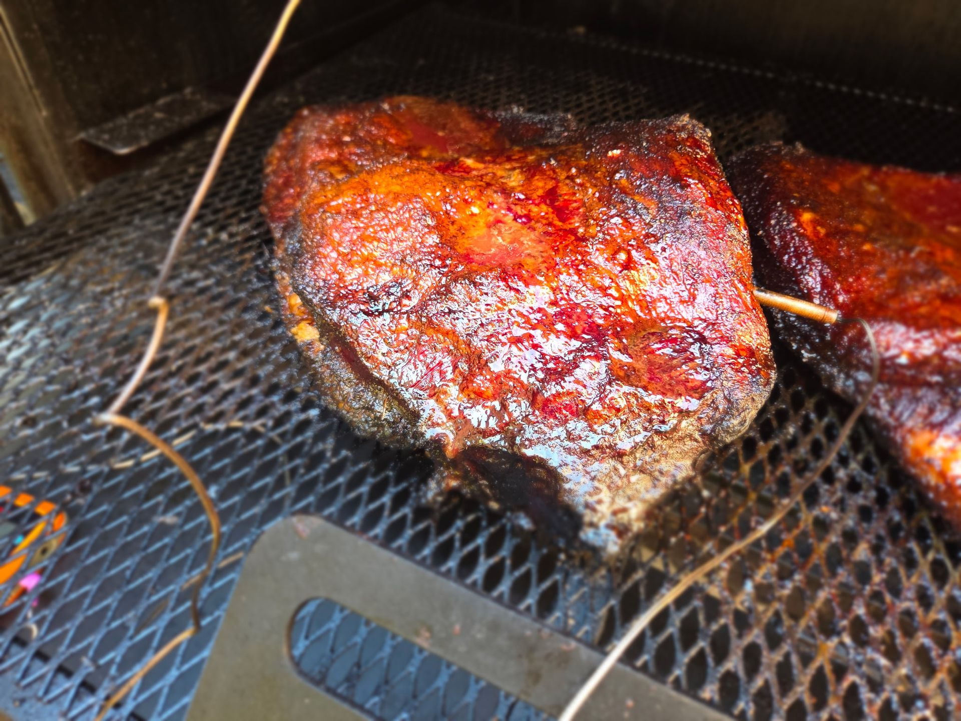 Smoked pork shoulder on a metal rack inside a smoker, with a temperature probe inserted.