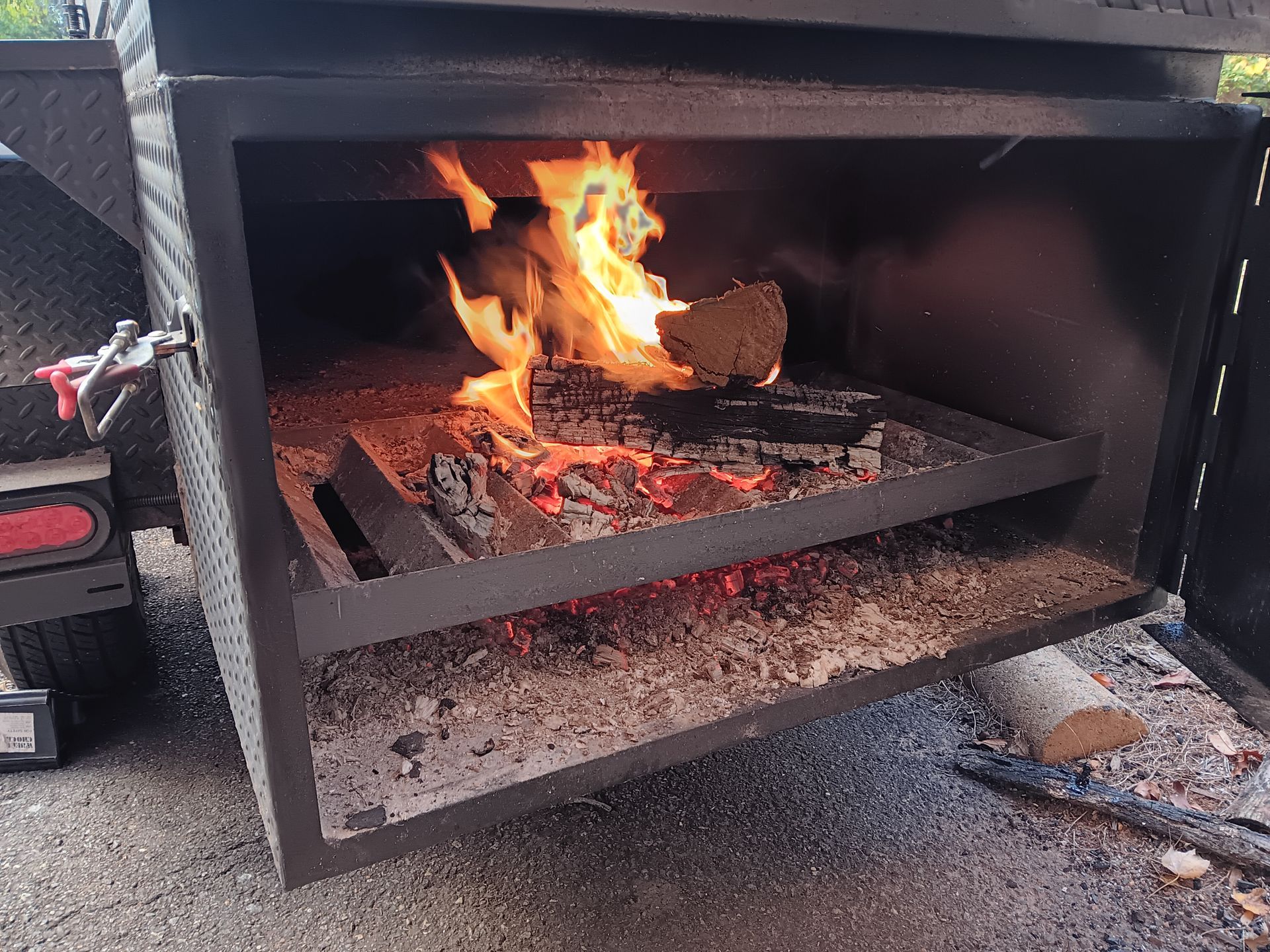 Fire burning in a large, metal smoker with a grill.
