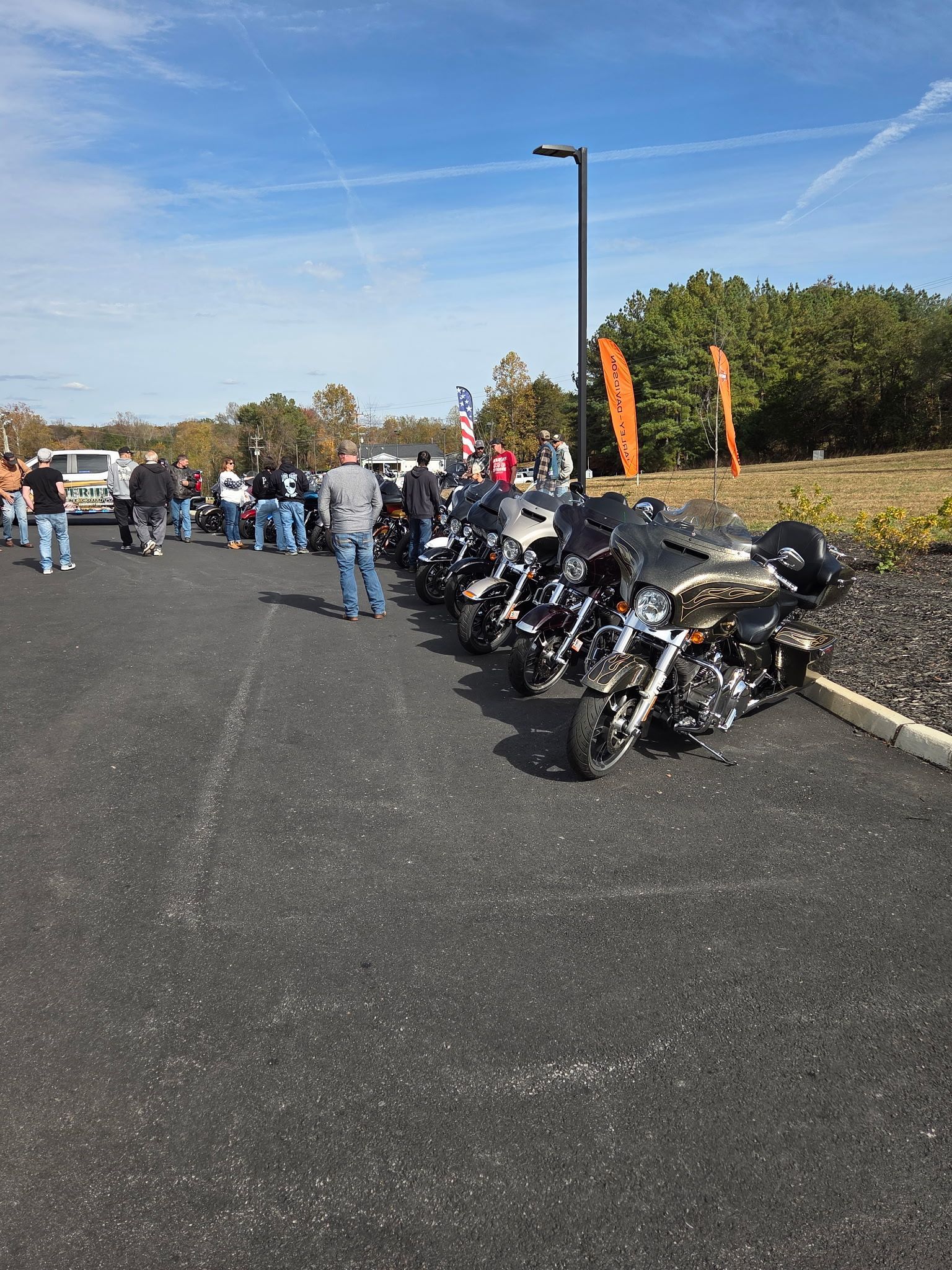 Motorcycles parked on asphalt, people walking nearby. Bright sunny day, blue sky.