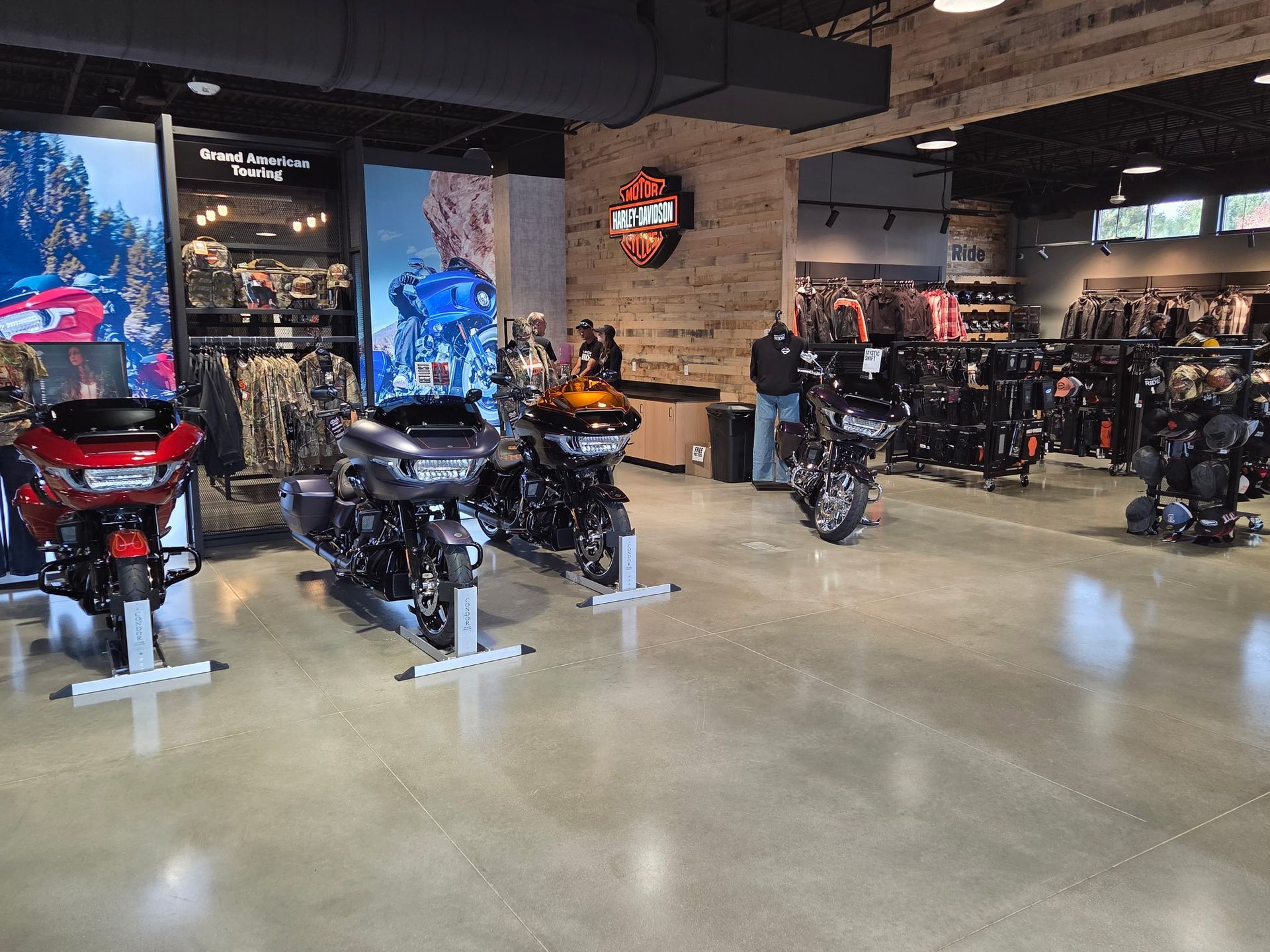 Motorcycle showroom with three motorcycles on display. Clothing racks and Harley-Davidson logo visible.