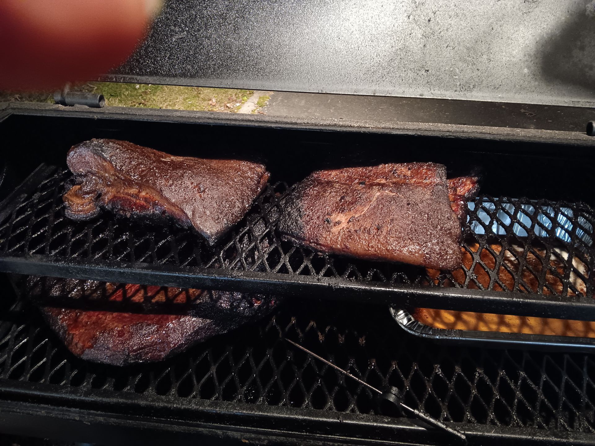 Smoker with three pieces of meat and a pan of beans on racks.