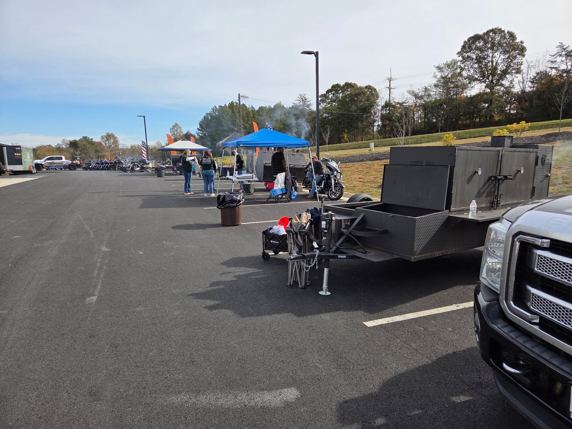 A parking lot with food vendors cooking outside, smoker trailer in foreground.