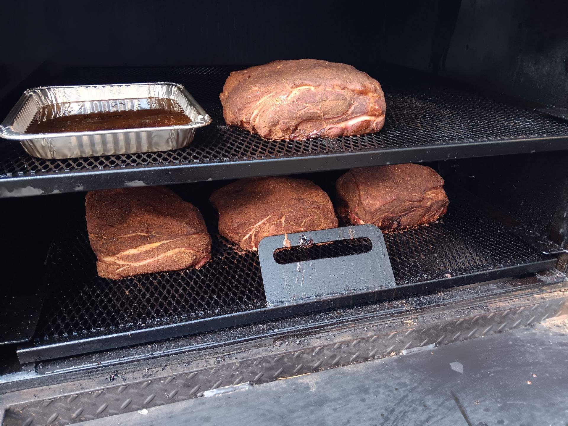 Smoker with seasoned meat on racks, plus a foil pan of liquid.