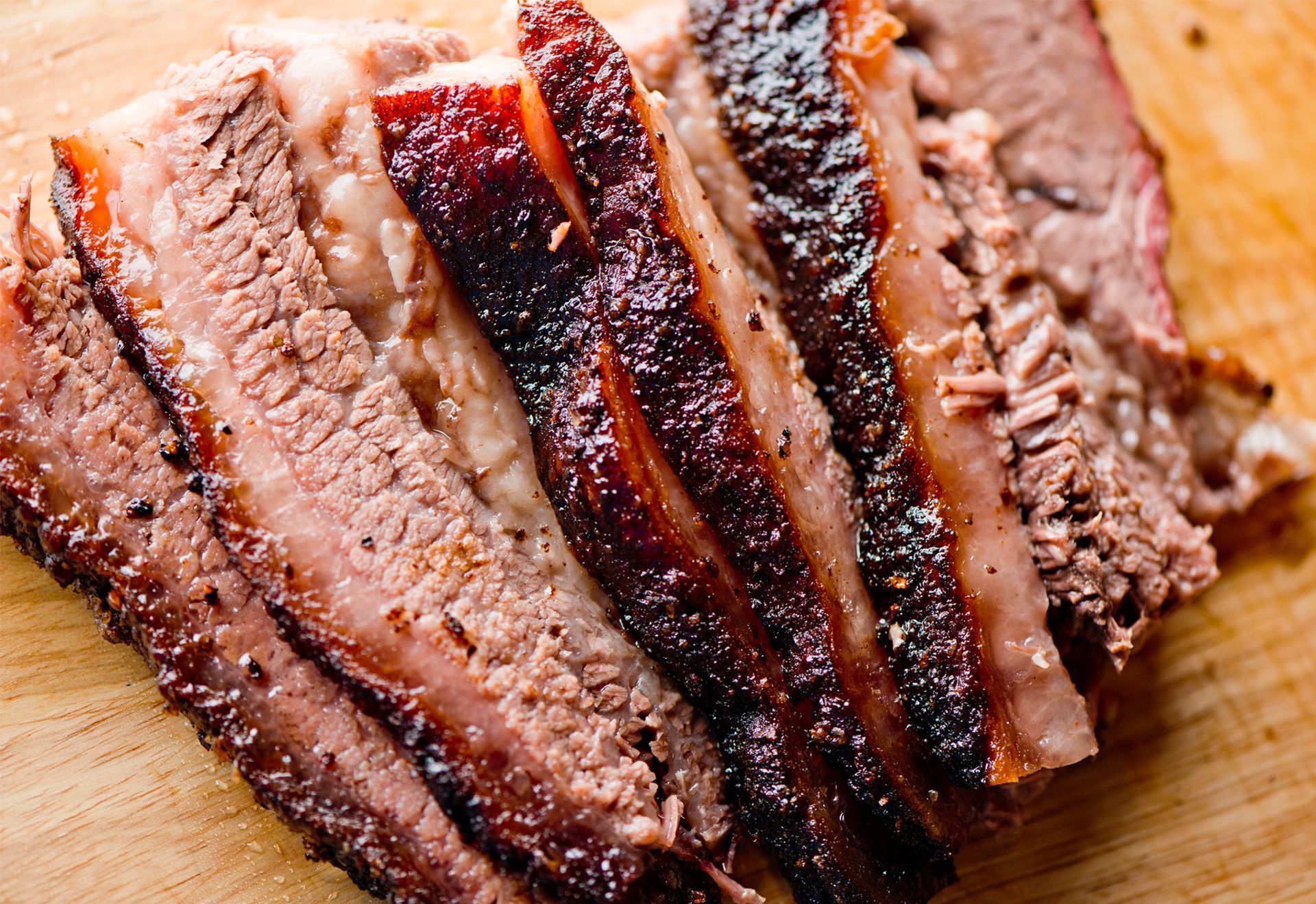 Sliced brisket on a wooden cutting board, with dark bark and pinkish-brown meat.