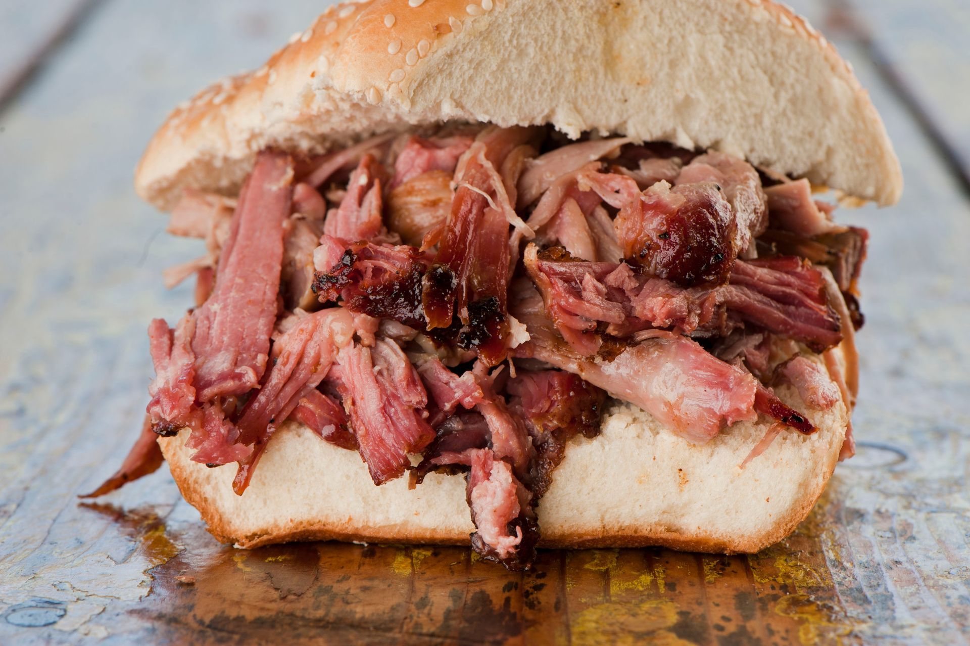 Pulled pork sandwich with sesame seed bun, close-up view on a blue wood table.