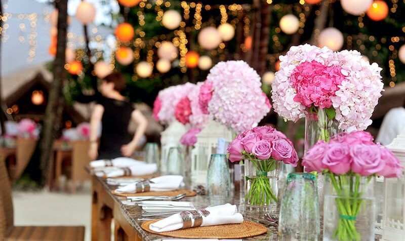A long table with pink flowers in vases on it.