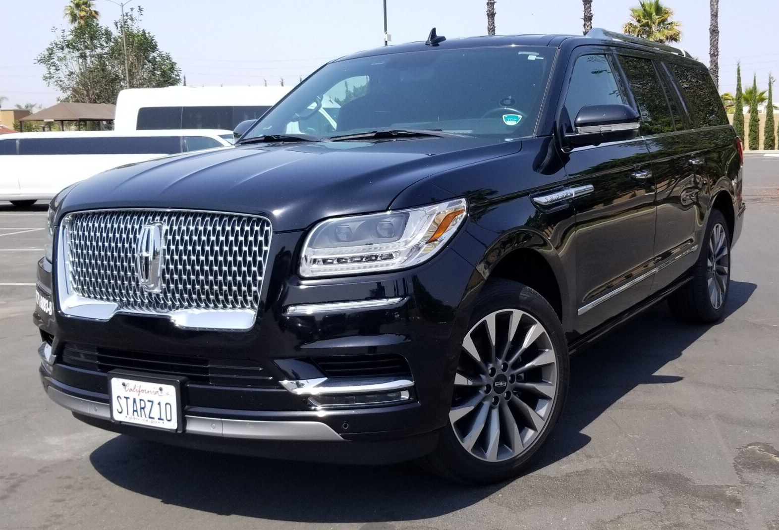 A black lincoln navigator is parked in a parking lot next to a white limousine.
