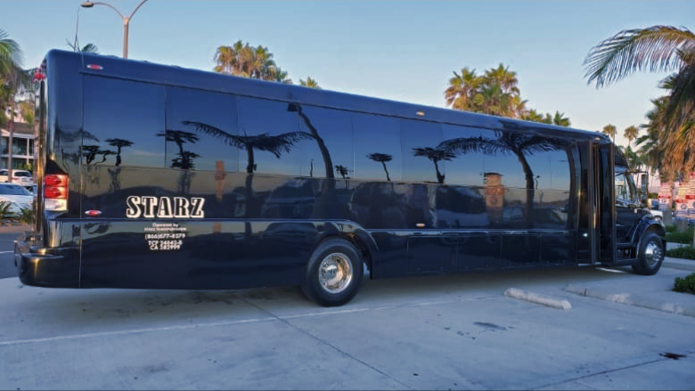 A black shuttle bus is parked in a parking lot with palm trees in the background.