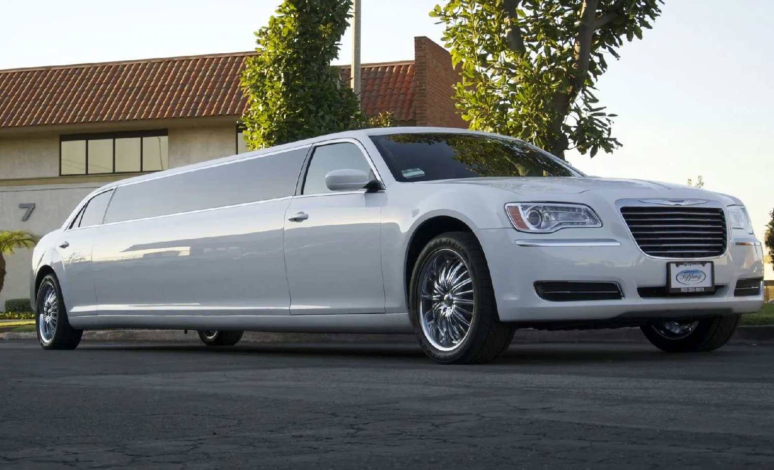 A white limousine is parked on the side of the road in front of a building.