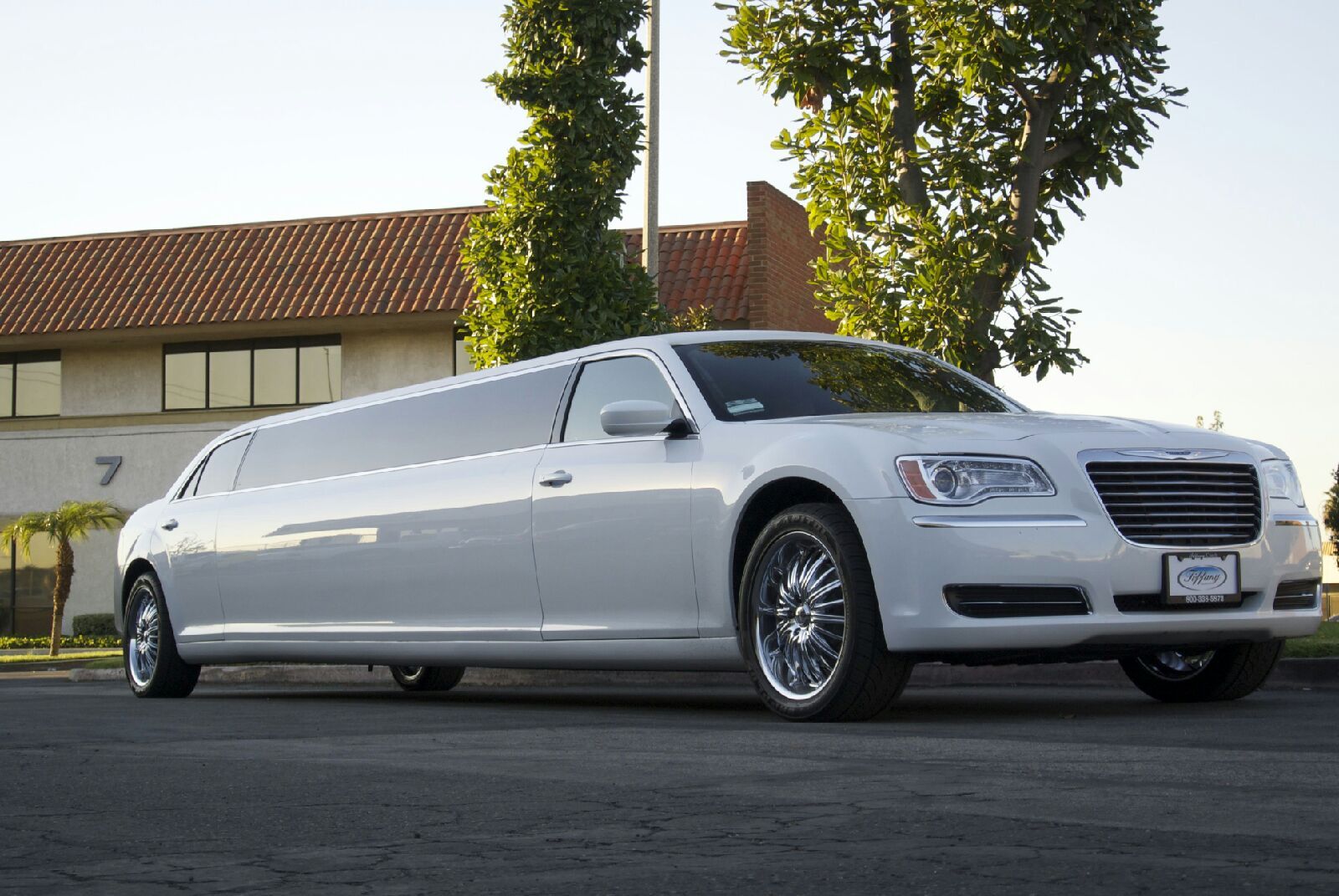 A white limousine is parked in front of a building
