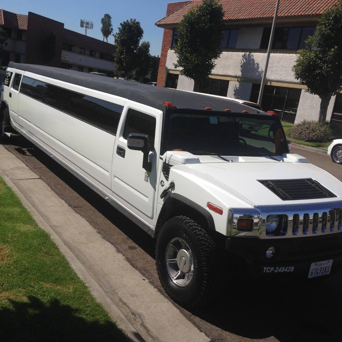 A white hummer limousine is parked on the side of the road