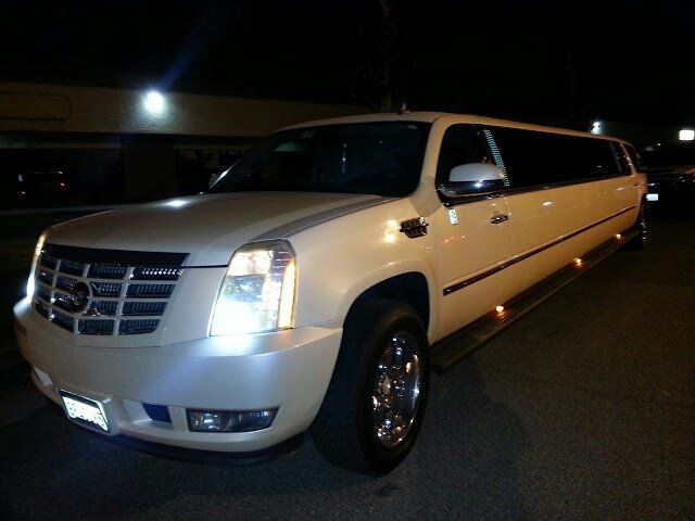 A white limousine is parked in a parking lot at night
