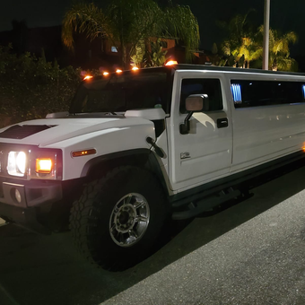 A white hummer limousine is parked on the side of the road at night