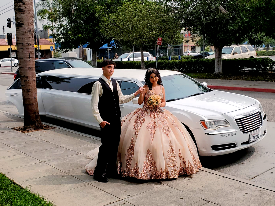 A bride and groom are posing for a picture in front of a white limousine.