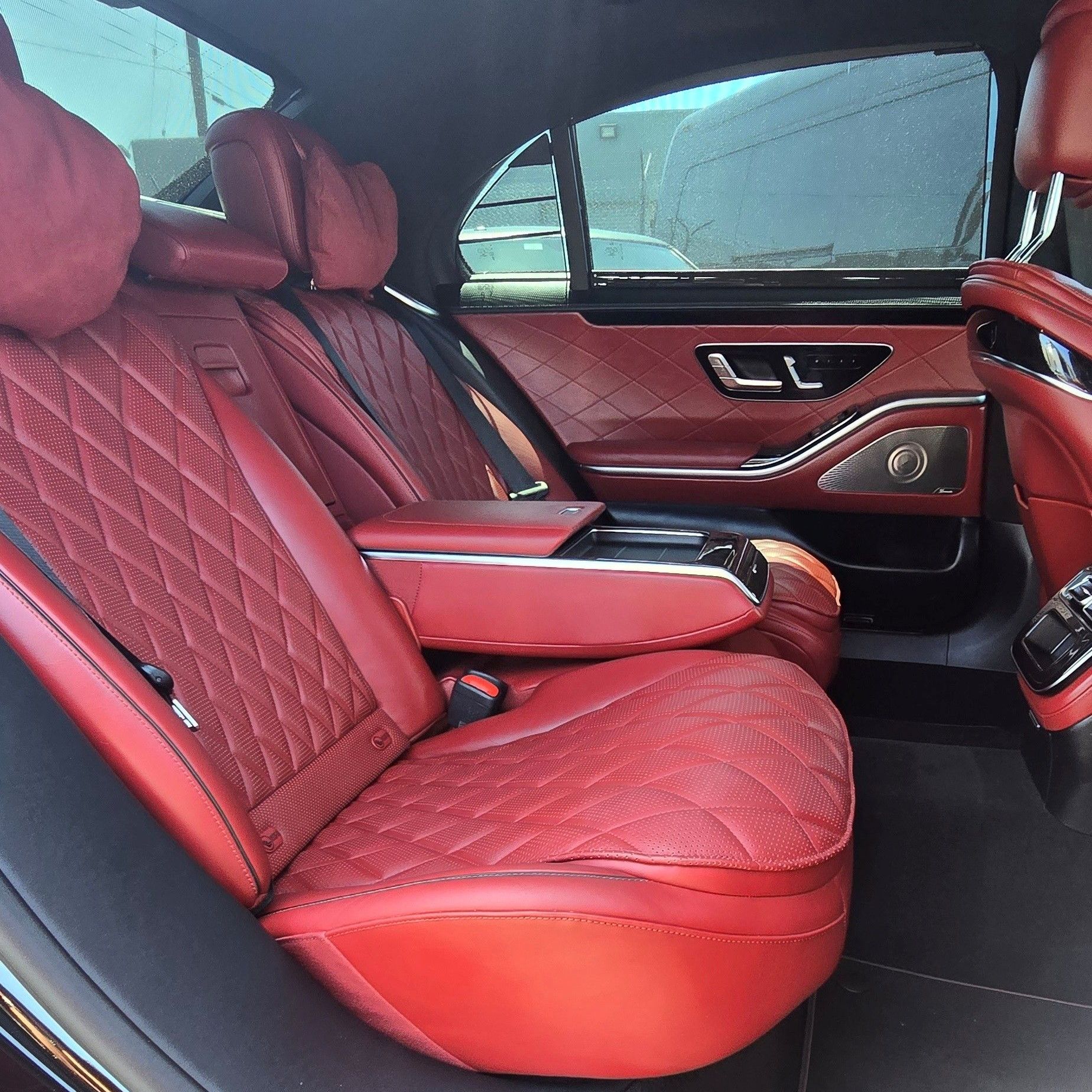 The back seats of a mercedes benz s class are black leather and have seat belts.