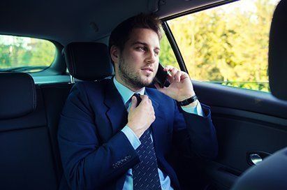 A man in a suit and tie is sitting in the back seat of a car talking on a cell phone.