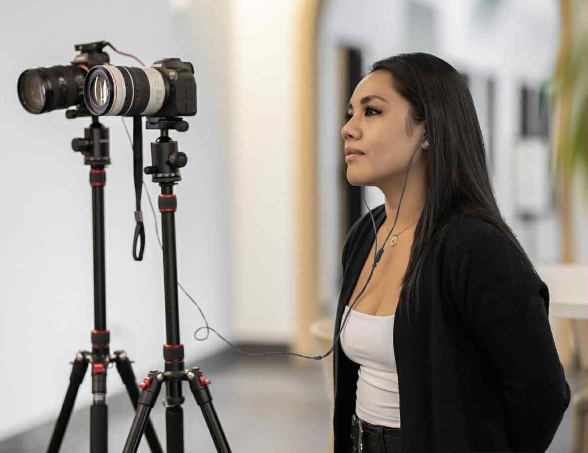 Woman standing beside cameras on tripods in a bright indoor hallway