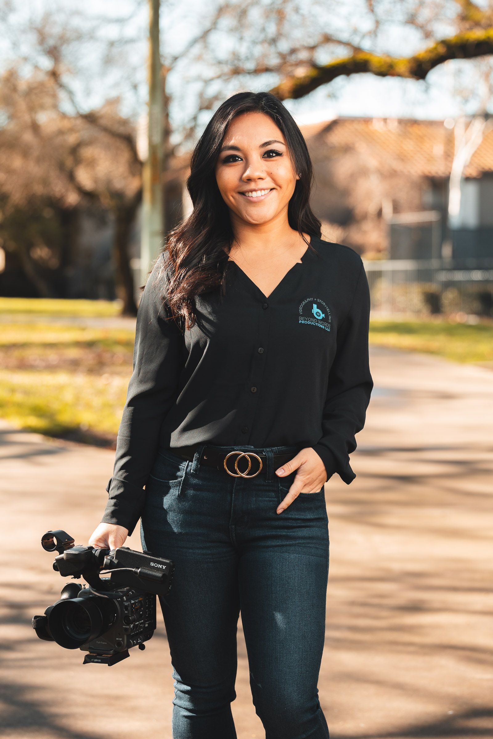A woman in a black shirt and jeans is holding a camera.
