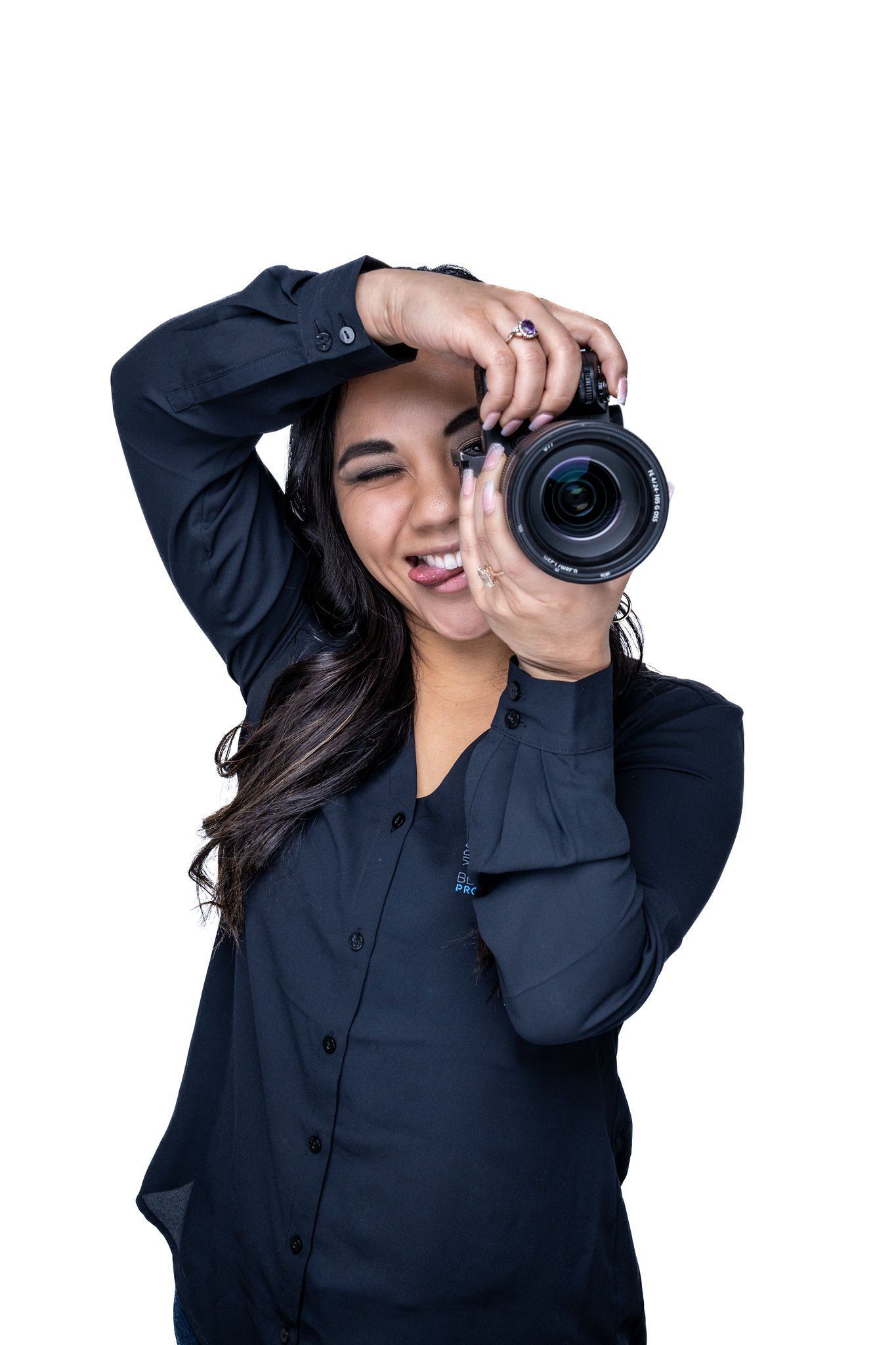 Woman holding camera, smiling, taking photo. Black button-down shirt.