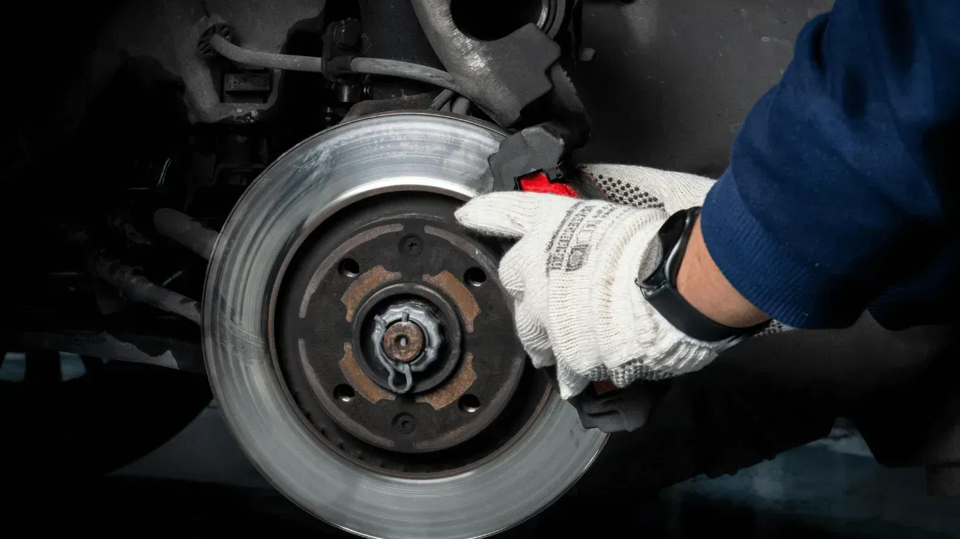 A mechanic in white gloves works on a car's brake rotor assembly in a workshop.
