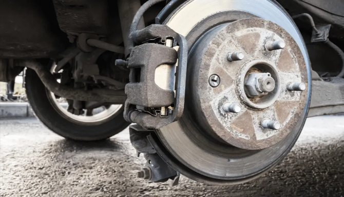 A close-up of a vehicle's disc brake assembly and wheel hub, showing the metal rotor, brake caliper, and wheel studs.