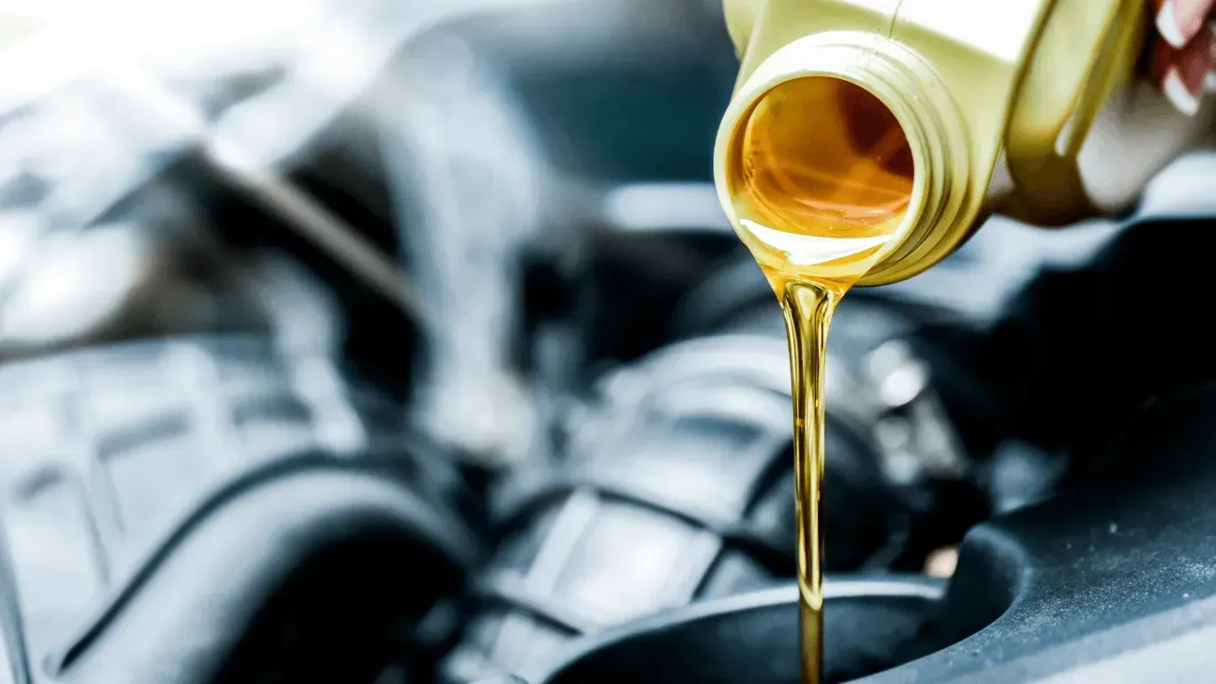 Golden motor oil being poured from a plastic container into a car engine.