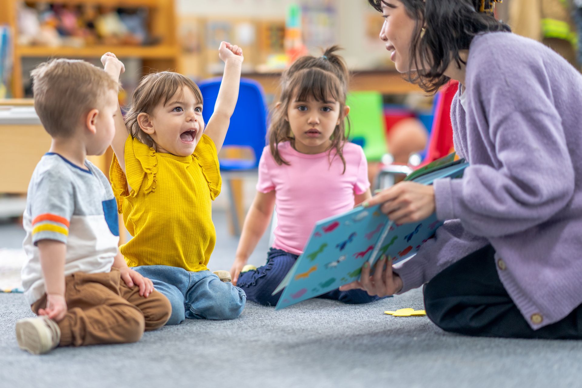 A teacher sits on the floor showing a book to three children, highlighting professional child care. A teacher sits on the floor showing a book to three children, highlighting professional child care.