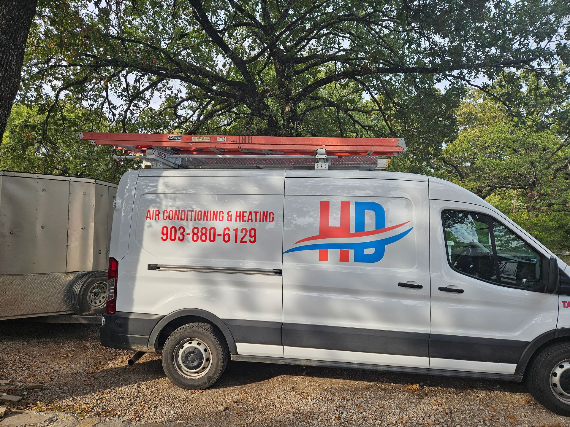 A white van with a ladder on top of it is parked in a parking lot.